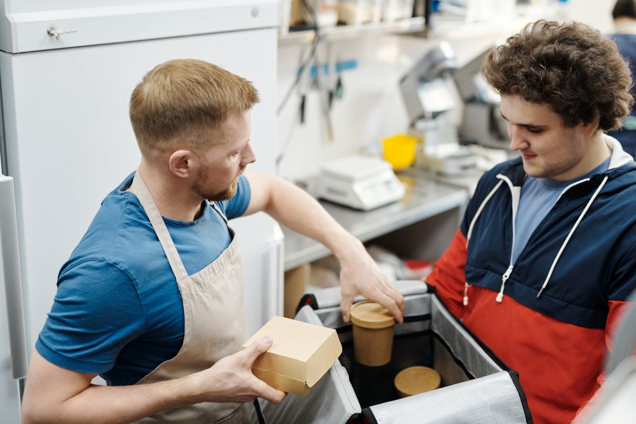 Two young men preparing food delivery orders in a small business kitchen.