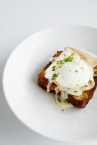 A delicious gourmet toast topped with poached egg and creamy sauce on a white plate.